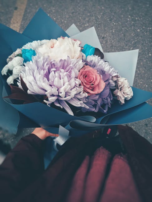 A fresh floral bouquet arranged with a mix of pink, white, purple, and blue flowers, including a prominent pink rose, white chrysanthemums, purple lisianthus, and bright blue accent flowers. The bouqu